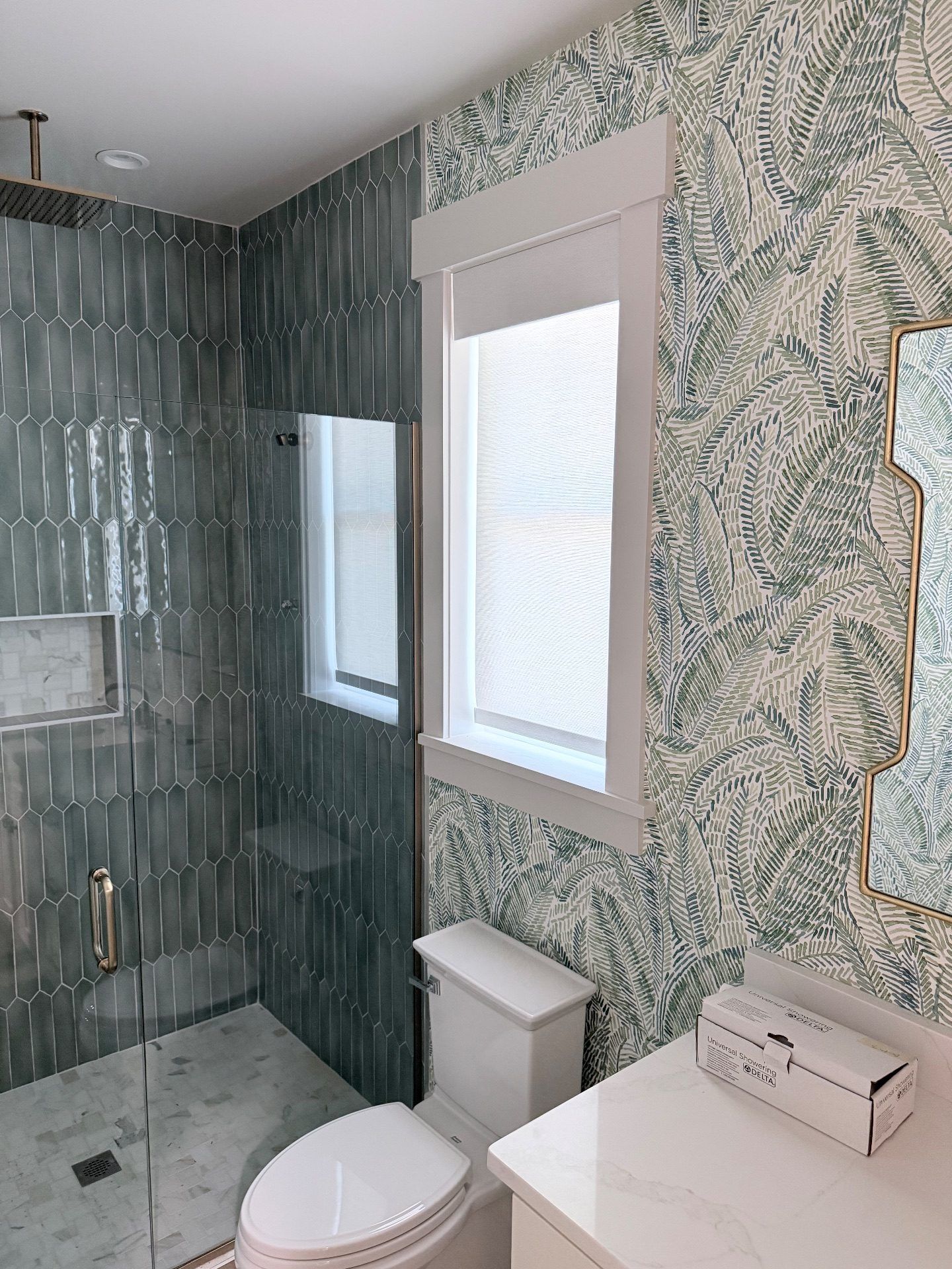Coastal green and blue wallpaper with a white roller shade in a bathroom