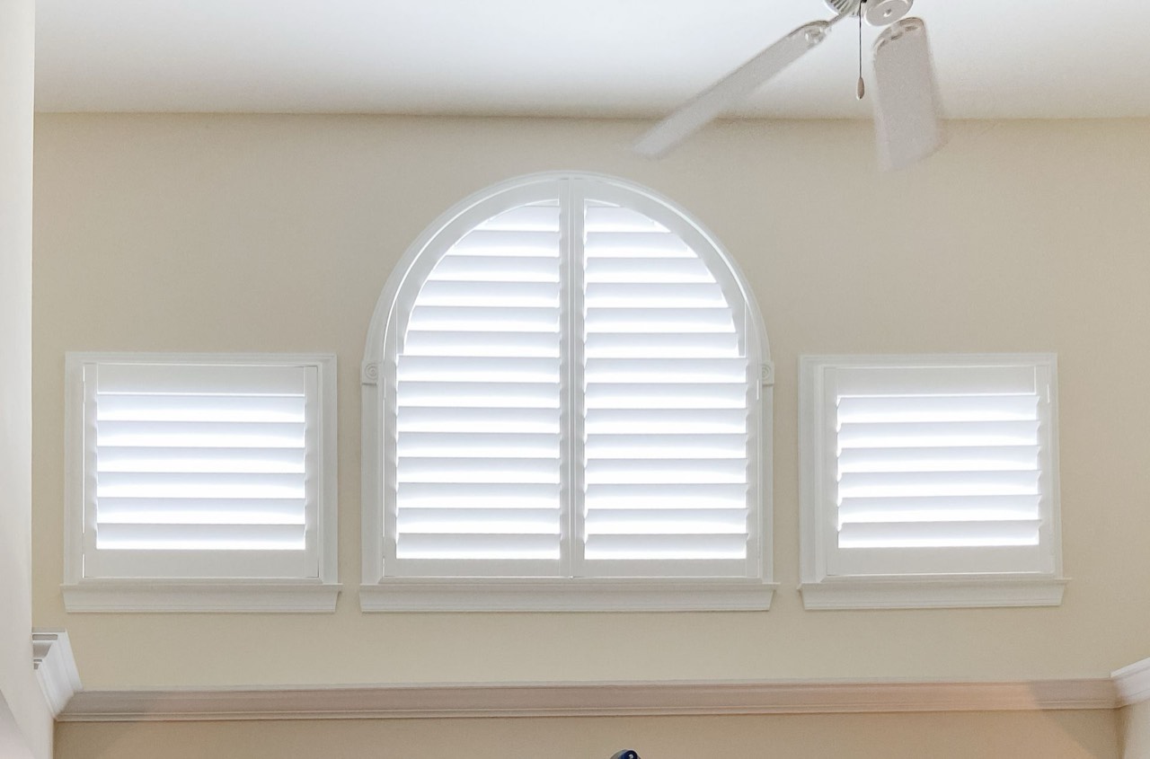 Custom arch-top plantation shutters, center-open, in a coastal home.